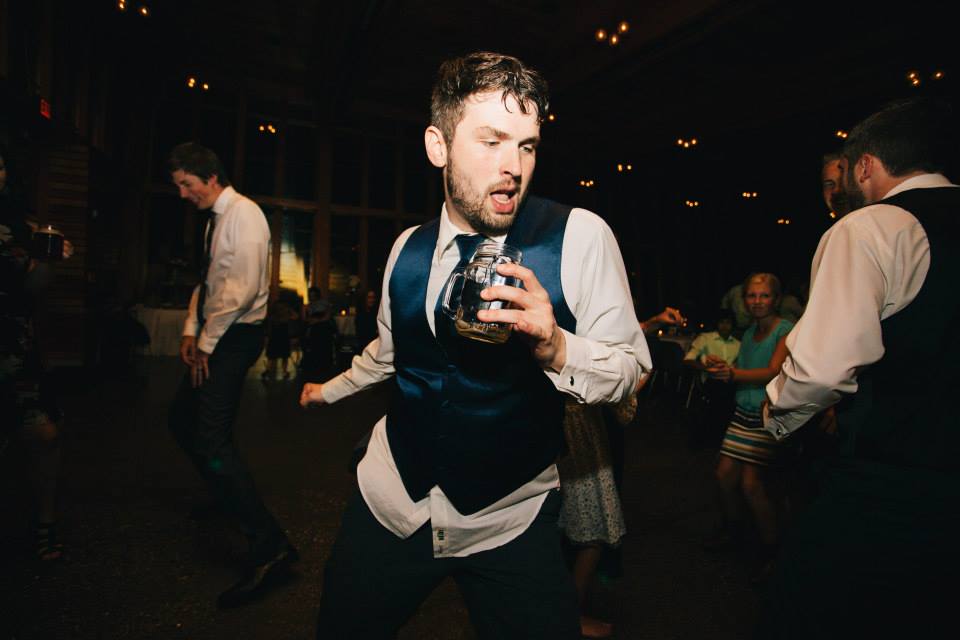 A photo of a young man dancing while holding a drink at a wedding reception